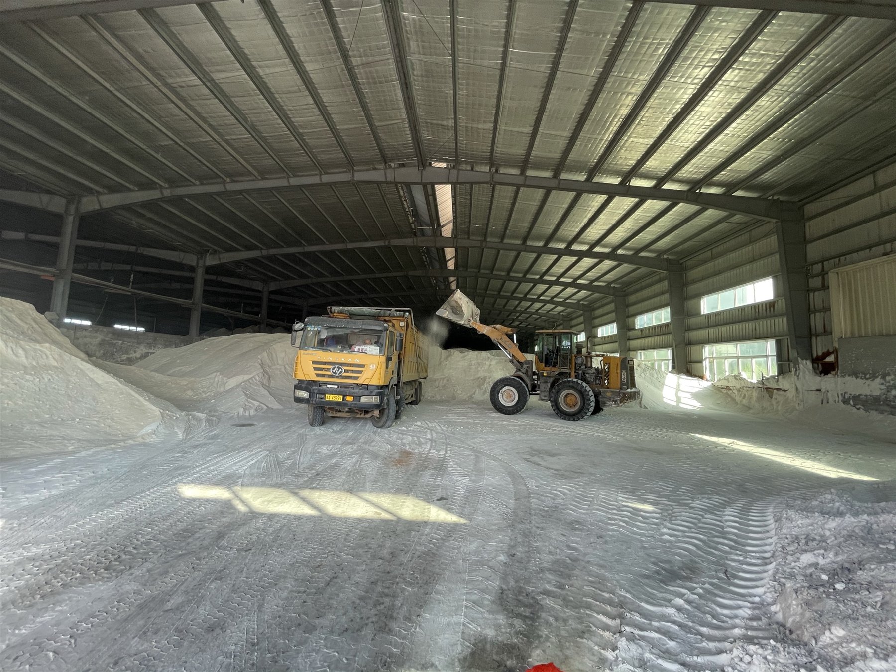 Warehouse loading operation with fertilizer stockpiles, loader and truck